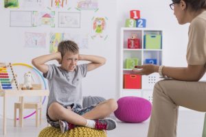 Self Regulation and Alertness Angry kid covering his ears during therapy with in room with toys